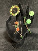 All six pieces displayed on jewelry hand stand on black background showing brooches, bracelet, earrings, necklace pendant and chain.