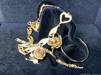 Five-piece lot of vintage costume jewelry including a rose brooch, a filigree tiger's eye brooch, Liz Claiborne necklace, rhinestone bracelet, and bangle arranged on black display hand