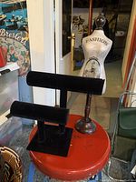 Two black velvet T-bar jewelry holders on a red round table, showing shapes and material.