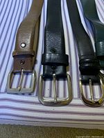 Close-up view of belt buckles showing three belts: two brown and one black, with square and rectangular silver buckles.