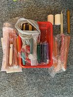 Basket containing assorted colorful candlesticks of different sizes and colors, some wrapped in plastic.