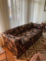 Side view of the floral patterned full length sofa showing the armrest and cushions.