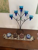 Full view of the blue glass tealight candle holder with five arms and the silver-plated tray with decorative items including cones and spheres on a wooden surface.