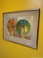 Framed print showing two stylized figures holding umbrellas in yellow-green and orange-red hues, hung on a yellow wall.