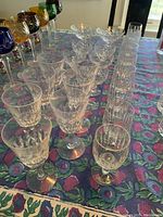 Photo showing multiple rows of crystal stemware on a tablecloth with a floral pattern including colored and clear glasses
