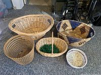 Photo of five wicker baskets arranged on carpet, showing size and style variations from large patterned to small and plain baskets.