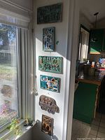 Six ceramic wall hangings mounted vertically on a white wall next to a window, showing their relative sizes and placement.