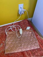 Small brown quilted heating pad plugged in with wired controller showing the unit powered on.