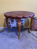 Front view of the wooden side table showing scalloped edges and cabriole legs on carpeted floor.
