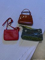 Three purses laid out on striped fabric: red, orange, and green, showing overall shape and size differences