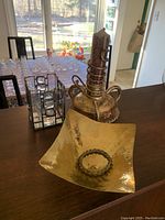 Tall gold-coloured ornate candle holder next to gold-coloured decorative bowl