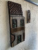 Two views of the two piece house wall art mounted on textured wall showing detail of roof tiles, windows, and balcony.