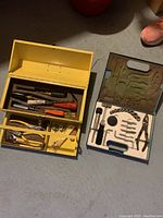 Two small tool kits side by side on floor, yellow metal toolbox and blue plastic case, each containing various hand tools