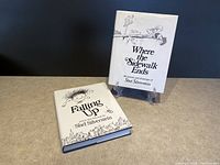 Photo showing both hardcover books with dust jackets: 'Where the Sidewalk Ends' standing on back with cover facing forward, 'Falling Up' lying flat with cover visible