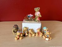 Cherished Teddies collection of 6 baby teddy magnets and 1 figurine, arranged on a table with red background.