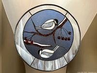 Front view of round stained glass window panel showing chickadee birds perched on brown branches with red berries and marbled white outer ring.