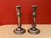 Pair of silver Empire style candlesticks against red background, showing overall shape and size without candles.