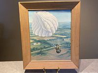 Front view of framed oil painting showing parachutist descending over farmland