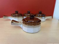 Four French onion soup bowls with lids, arranged on a wooden surface against a red wall, showing top and angled side views.