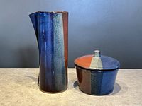 Photo showing front angle of the tall pottery vase with spout and lidded pottery bowl, highlighting glaze colors and shape.