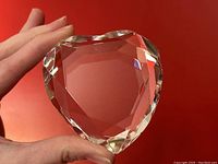 Front view of heart-shaped Rosenthal lead crystal paperweight held in hand against red background showing clarity and facet details.