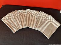 Eight natural cotton napkins fanned out, showing consistent woven checkered and striped border pattern.