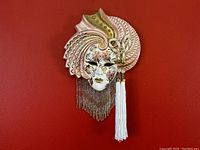 Front view of the hand-painted porcelain Venetian mask with floral and gold decorations, bead fringe, and tassels.