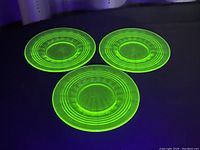 Three translucent green uranium glass plates glowing under UV light, showing bright fluorescent green color.