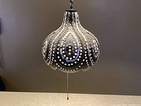 Front view of black fat lava style ceramic pendant swag lamp with decorative perforations and pull chain.