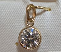 Close-up front view of round moissanite pendant in 10K gold bezel setting highlighting the gemstone's facets.