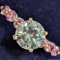 Close-up of round green moissanite center with pink lab diamonds on band.