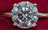 Close-up top view of round brilliant cut lab-grown diamond in four-prong setting against red background