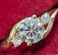 Angled close-up of ring face on red background showing center and side diamonds in gold setting