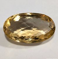 Close-up photo of the oval faceted citrine gemstone showing its color, clarity, and faceting details on a white background.