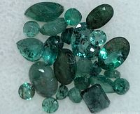 Assortment of green faceted emeralds on white foam background.