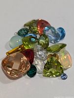 Photo of the assortment of various genuine faceted and polished gemstones of multiple colors and shapes.