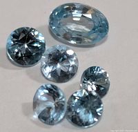 Six genuine blue zircon gemstones in varying shapes and sizes, light to medium blue color, faceted cuts, arranged on a neutral background.