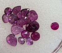 Close-up of assorted faceted rubies and amethysts on white background showing variety of shapes and sizes