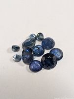 Photo showing loose genuine sapphire gemstones of different cuts and sizes on a plain surface.