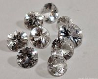 Cluster of 10 loose white sapphire round cut gemstones showing clarity and faceting.
