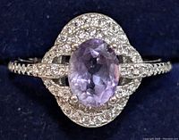 Top view of the silver ring showcasing the oval faceted light purple amethyst center stone surrounded by two rows of small clear cubic zirconia stones against a dark background.