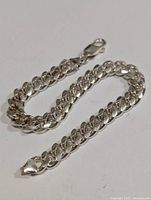 Silver curb chain bracelet arranged to show entire length and clasp.