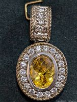 Close-up front view of silver pendant with oval yellow citrine gemstone and surrounding clear CZ stones, showing detail of bail decorated with small CZ stones and rope edging.