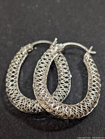 Pair of silver hoop earrings with intricate lattice pattern set on a black background, showing top down view.