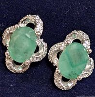 Close-up of the front of the pair of silver earrings, showing oval emerald stones and surrounding cubic zirconia decoration.