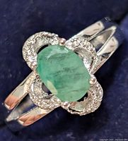 Close-up photo of the silver ring showing the oval green emerald center stone and surrounding cubic zirconia stones on a split shank band.