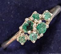 Close-up image of a silver ring with a cluster of round emerald stones of various sizes set on the face.