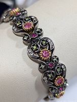 Close-up angled view of the silver bracelet showing pink, green, and clear stones with gold-tone bezels and oxidized silver metal.