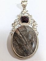 Front view of the silver pendant showing large oval stone with natural patterns and faceted square stone in silver floral setting