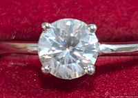 Close-up of the front view of the silver ring with the round moissanite stone in a four-prong setting against a red background.